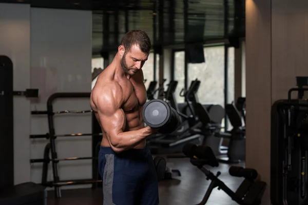 Homem no ginásio que exercita bíceps com halteres — Fotografia de Stock