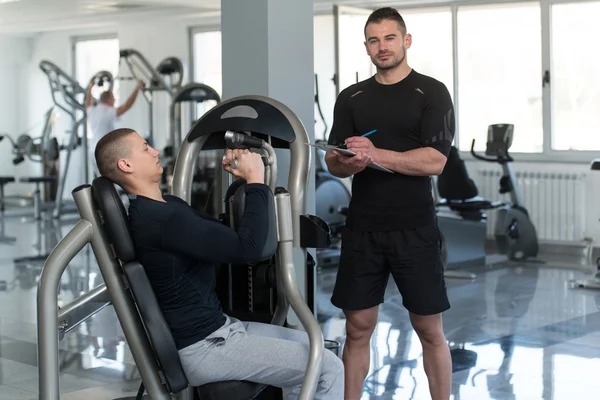 Personal Trainer toma notas enquanto homem exercitando peito — Fotografia de Stock