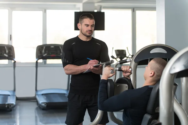 Personal Trainer prende appunti mentre l'uomo esercizio petto — Foto Stock