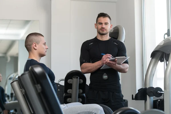 Personal Trainer neemt notities terwijl Man uitoefening van benen — Stockfoto