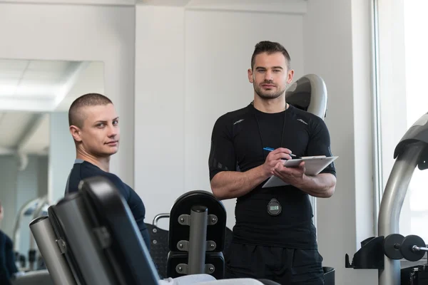 Personal Trainer Takes Notes While Man Exercising Legs — Stock Photo, Image