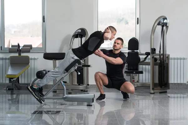 Treinador de ginástica ajudando o jovem no exercício de volta — Fotografia de Stock