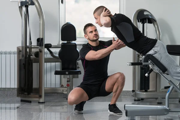 Uomo treno indietro sulla macchina con personal trainer — Foto Stock