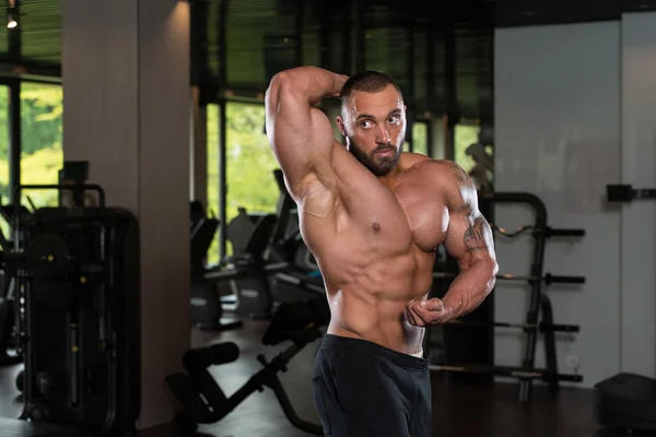 Fitness geformter Muskelmann posiert in dunkler Turnhalle — Stockfoto