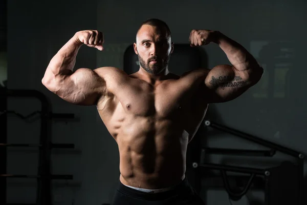 Fitness en forma de hombre muscular posando en el gimnasio oscuro —  Fotos de Stock