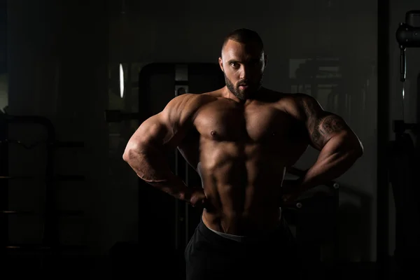 Fitness en forma de hombre muscular posando en el gimnasio oscuro —  Fotos de Stock