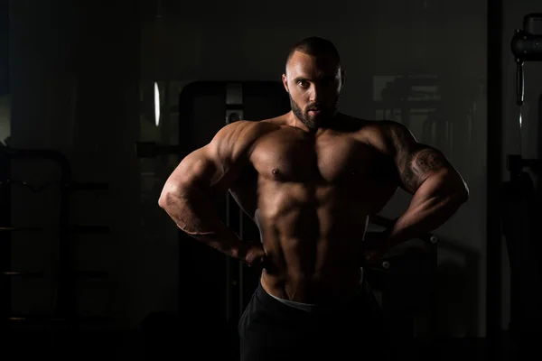 Aptidão em forma de homem do músculo posando no ginásio escuro — Fotografia de Stock