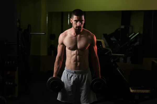 Homem no ginásio que exercita bíceps com halteres — Fotografia de Stock