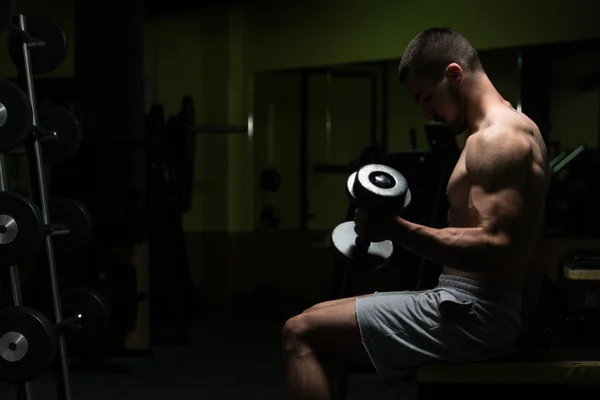 Młody człowiek z hantlami ćwiczenia bicepsów — Zdjęcie stockowe