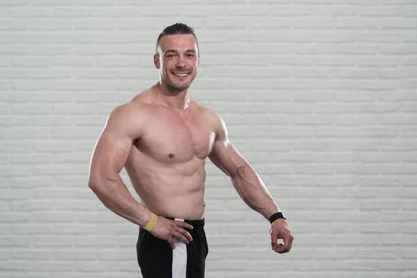 Svalnatý muž protahuje svaly na pozadí bílé cihly — Stock fotografie