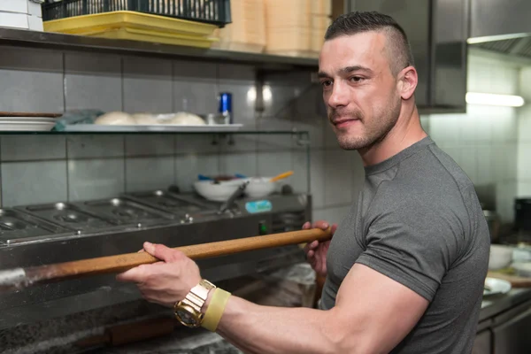 Giovane uomo che mette la pizza nel forno — Foto Stock