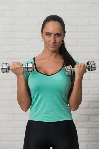 Mujer atractiva ejercitando bíceps sobre fondo de ladrillos blancos —  Fotos de Stock