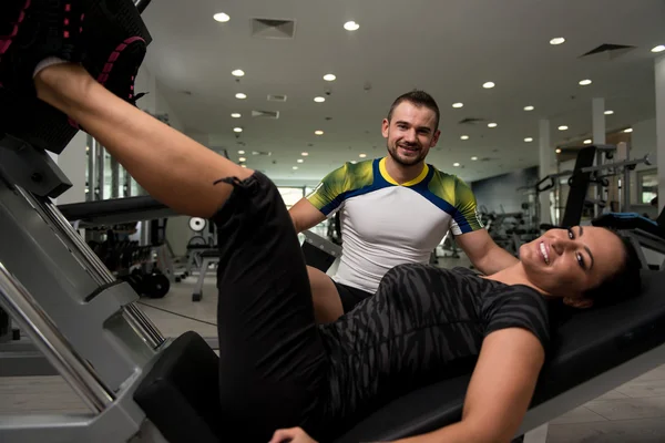 Frau trainiert Beine an Maschine mit Personal Trainer — Stockfoto