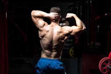 Spor salonunda güçlü duran ve kaslarını esneten yakışıklı adam - kaslı atletik vücut geliştirici spor sonrası vücut geliştirme modeli pozu