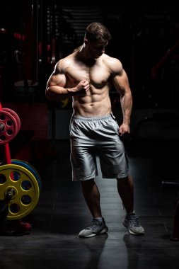 Spor salonunda güçlü duran ve kaslarını esneten yakışıklı adam - kaslı atletik vücut geliştirici spor sonrası vücut geliştirme modeli pozu