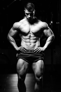 Spor salonunda güçlü duran ve kaslarını esneten yakışıklı adam - kaslı atletik vücut geliştirici spor sonrası vücut geliştirme modeli pozu