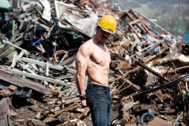 Eski Hurda Metal Garajında Güçlü Duran Genç Adam ve Esnek Kaslar - Kaslı Atletik Vücut Geliştirici Spor Modeli Sarı Miğferli Pozisyon