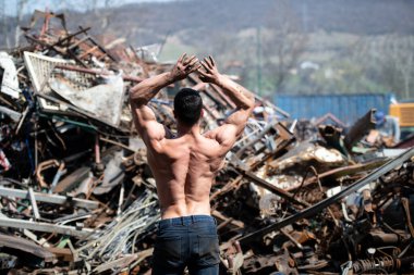 Fiziksel olarak fit genç bir adamın portresi Endüstriyel Hurda Bahçesinde duruyor İyi eğitilmiş vücudunu gösteriyor