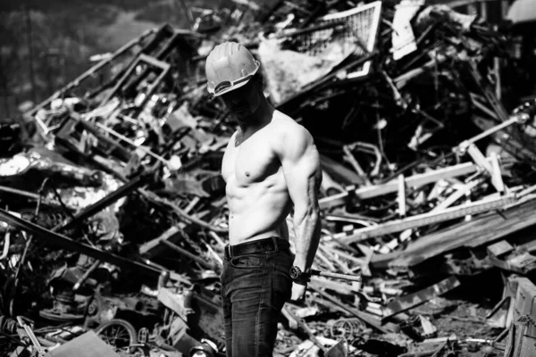 Young Man Standing Strong in Old Scrap Metal Garage and Flexing Muscles - Muscular Athletic Bodybuilder Fitness Model Posing