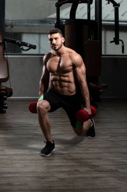 Spor salonundaki güçlü adam dambıllarla bacak egzersizi yapıyor kaslı atletik vücut geliştirici spor mankeni egzersizi.