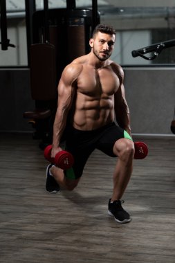 Spor salonundaki güçlü adam dambıllarla bacak egzersizi yapıyor kaslı atletik vücut geliştirici spor mankeni egzersizi.