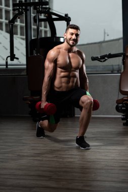 Spor salonundaki güçlü adam dambıllarla bacak egzersizi yapıyor kaslı atletik vücut geliştirici spor mankeni egzersizi.