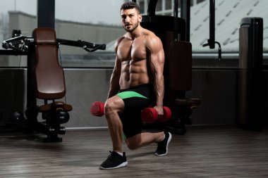 Spor salonundaki güçlü adam dambıllarla bacak egzersizi yapıyor kaslı atletik vücut geliştirici spor mankeni egzersizi.