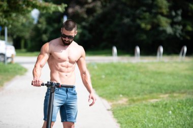 Genç Adam Scooter 'a bindikten sonra dinleniyor. Şehirde cadde boyunca.