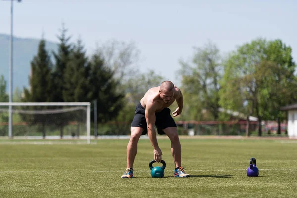 ケトルベル屋外とフレキシングな筋肉を持つ男の運動 筋肉運動体ビルダーフィットネスモデルの演習 — ストック写真