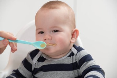 Anne, bebeğini kaşıkla besliyor. Anne, sevimli çocuğuna sağlıklı yiyecekler veriyor.