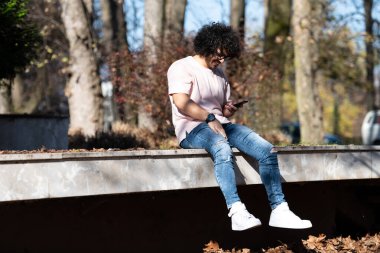 Yakışıklı Afro Adamın Dokunaklı Konuşan Portresi ya da Sonbaharda Arama ve Oturma İçin Akıllı Telefon Kullanımı