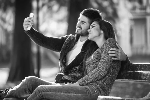 Young Couple Sitting Bench Beautiful Autumn Day Taking Selfie Park —  Fotos de Stock
