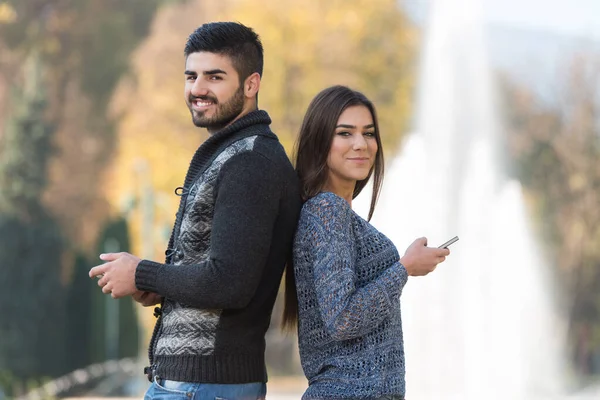 Ungt Par Holder Ser Mobiltelefon Udendørs Parken - Stock-foto