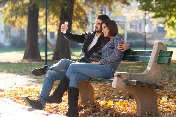 Young Couple Sitting Bench Beautiful Autumn Day Taking Selfie Park — Fotografia de Stock