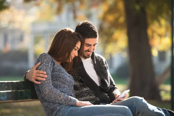 Young Couple Sitting Bench Beautiful Autumn Day Typing Phone Park — 스톡 사진