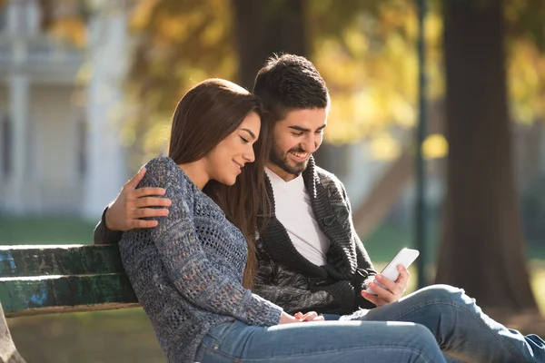 Young Couple Sitting Bench Beautiful Autumn Day Typing Phone Park — 图库照片