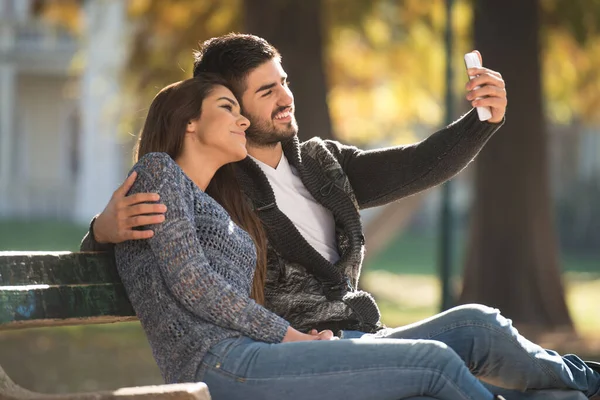 Young Couple Sitting Bench Beautiful Autumn Day Taking Selfie Park — ストック写真
