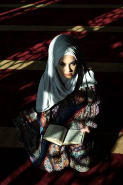 Diz çöküp Kuran okuyan ve kitabın sayfasını çeviren güzel Müslüman kadın.