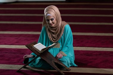 Diz çöküp Kuran okuyan ve kitabın sayfasını çeviren güzel Müslüman kadın.