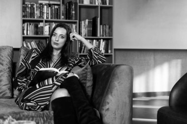 Kütüphanedeki Koltukta oturan Siyah Saçlı Güzel Kadın - Arka tarafta Bulanık Kitaplar