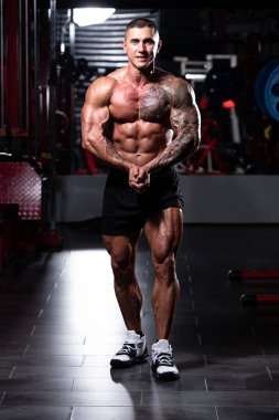 Spor salonunda güçlü duran ve kaslarını esneten yakışıklı adam - kaslı atletik vücut geliştirici spor sonrası vücut geliştirme modeli pozu