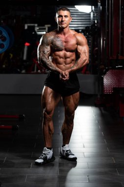 Spor salonunda güçlü duran ve kaslarını esneten yakışıklı adam - kaslı atletik vücut geliştirici spor sonrası vücut geliştirme modeli pozu