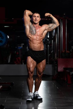 Spor salonunda güçlü duran ve kaslarını esneten yakışıklı adam - kaslı atletik vücut geliştirici spor sonrası vücut geliştirme modeli pozu