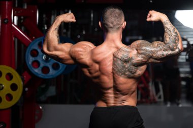 Spor salonunda güçlü duran ve kaslarını esneten yakışıklı adam - kaslı atletik vücut geliştirici spor sonrası vücut geliştirme modeli pozu