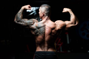 Spor salonunda güçlü duran ve kaslarını esneten yakışıklı adam - kaslı atletik vücut geliştirici spor sonrası vücut geliştirme modeli pozu