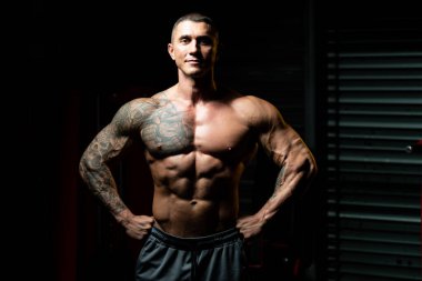 Spor salonunda güçlü duran ve kaslarını esneten yakışıklı adam - kaslı atletik vücut geliştirici spor sonrası vücut geliştirme modeli pozu