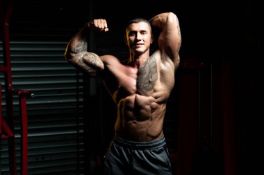 Spor salonunda güçlü duran ve kaslarını esneten yakışıklı adam - kaslı atletik vücut geliştirici spor sonrası vücut geliştirme modeli pozu