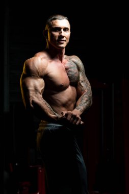 Spor salonunda güçlü duran ve kaslarını esneten yakışıklı adam - kaslı atletik vücut geliştirici spor sonrası vücut geliştirme modeli pozu