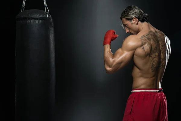 Boxeador muscular sin camisa con saco de boxeo en el gimnasio —  Fotos de Stock