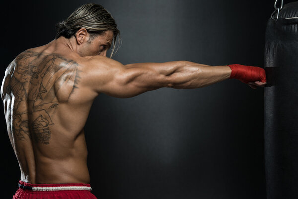 Мускулистый боксер без рубашки с боксерской грушей в спортзале
